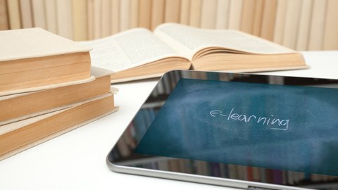 Foto: auf einem Tisch liegen vier Bücher sowie ein Tablet. Auf dem Bildschirm des Tablets ist das Foto einer Tafel zu sehen, auf der mit Kreide das Wort "e-learning" geschrieben steht.