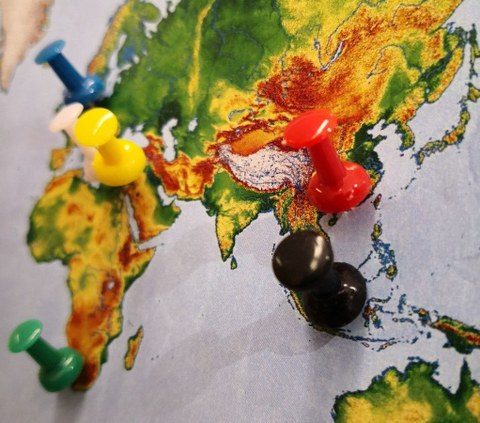 Foto: Nahaufnahme einer Weltkarte, in die farbige Stecknadeln gesteckt sind.