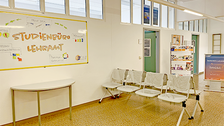 Foto eines Ganges im Seminargebäude 2. Im Vordergrund sind Sitzbänke und eine Tafel mit der Aufschrift "Studienbüro Lehramt" zu sehen. Im Hintergrund sind ein Aufsteller, Flyer und zwei Türen zu erkennen.