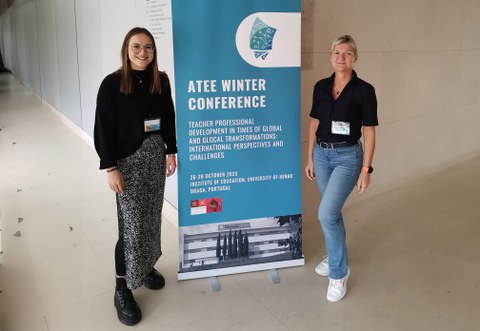 Zwei Frauen stehen links und rechts neben einem Roll Up, worauf Eckdaten zur ATEE Winter Konferenz zu sehen sind.