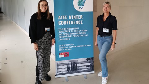 Zwei Frauen stehen links und rechts neben einem Roll Up, worauf Eckdaten zur ATEE Winter Konferenz zu sehen sind.