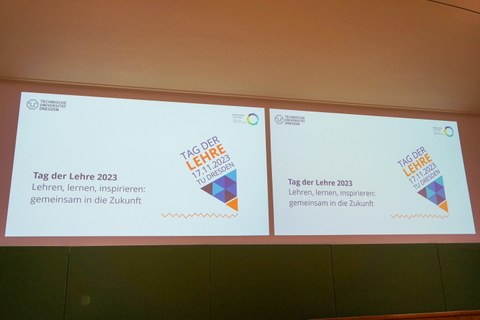 Auf dem Foto sind zwei Projektionsflächen zu sehen, die die Titelfolie einer Präsentation zeigen: "Tag der Lehre 2023, Lehren, lernen, inspirieren: gemeinsam in die Zukunft."