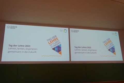 Auf dem Foto sind zwei Projektionsflächen zu sehen, die die Titelfolie einer Präsentation zeigen: "Tag der Lehre 2023, Lehren, lernen, inspirieren: gemeinsam in die Zukunft."