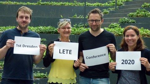 Foto von vier Personen, die jeweils ein Blatt Papier vor sich halten. Die aufschrift der vier Blätter ergibt zusammen den Text "1st Dresden LETE Conference 2020"