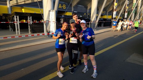 4 Personen in Sportklamotten nach einem Firmenlauf posierend vor einem Stadion