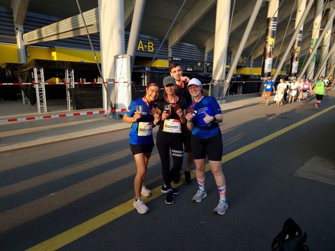 4 Personen in Sportklamotten nach einem Firmenlauf posierend vor einem Stadion