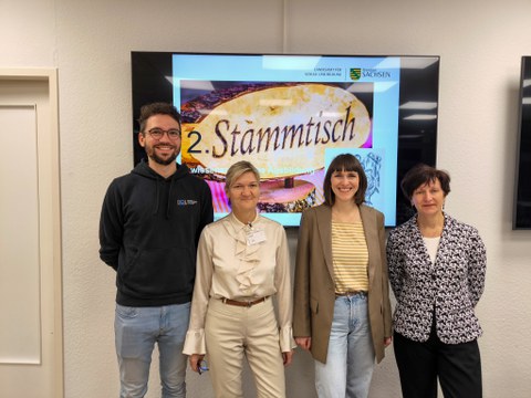 Gruppenbild mit 4 Personen vor einem großen Bildschirm