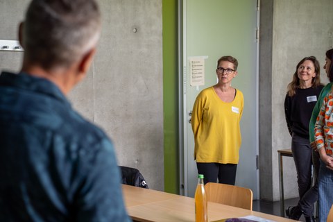 Mann hält Vortrag (von hinten fotografiert) Zuhörerinnen sind im Hintergrund zu sehen.
