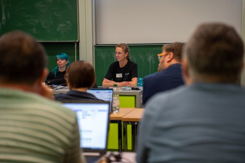 Zwei Frauen halten Vortrag und sitzen an einem Pult.