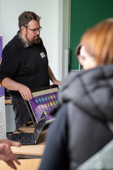 Mann zeigt etwas an einem Bildschirm und steht dabei.