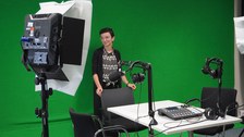 Frau steht vor Greenscreen und vor ihr ist Podcast-Technik zu sehen
