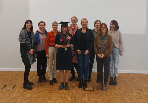 10 Personen stehen vor einer weißen Wand, die eine Präsentation zeigt.