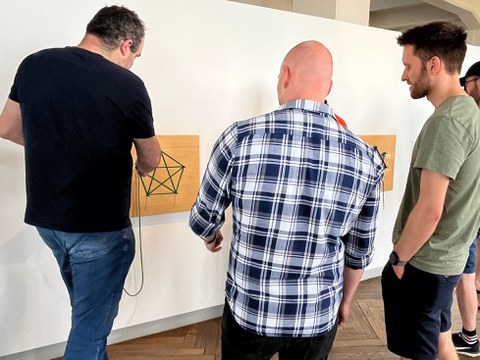 § Personen lösen ein Rätsel, das an einer Wand hängt. 