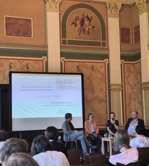 Zu sehen sind vier Personen, die in einem Museum auf einer Bühne eine Podiumsdiskussion führen