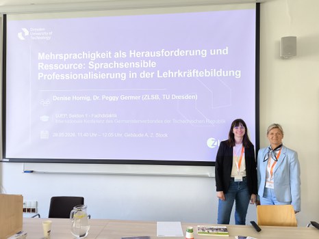 Zwei Frauen stehen vor einer Beamerleinwand, die eine Titelfolie einer Präsentation zeigt