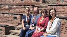 4 Frauen sitzen nebeneinander auf Stufen eines Amphitheaters