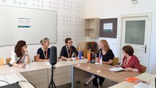 Fünf Personen sitzen nebeneinander an einem Ecktisch und sprechen miteinander
