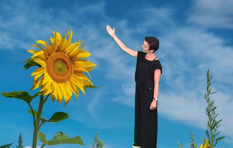 Frau steht vor einem digital eingefügten Hintergrund, der eine Sonnenblume zeigt und blauen Himmel zeigt.