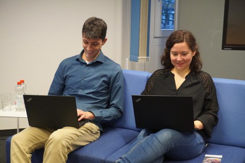 Frau und Mann sitzen jeweils mit Laptop auf dem Schoß auf einem Sofa.