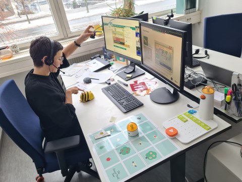 Frau sitzt vor PC am Schreibtisch und demonstriert informatische Lehrmittel in Videositzung