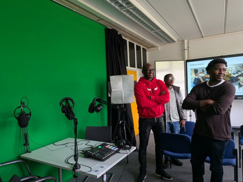 3 Personen stehen vor einem eingerichteten Podcast-Set-Up mit Greenscreen im Hintergrund