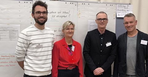 Gruppenbild mit 4 Personen vor einem Whiteboard