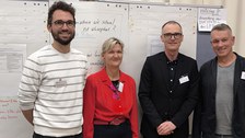 Gruppenbild mit 4 Personen vor einem Whiteboard