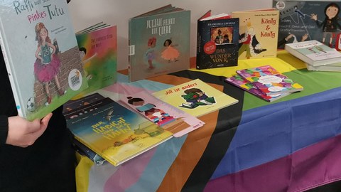 Zwei Personen stehen an einem Tisch gefüllt mit Schulbüchern für queere Grundschulkinder