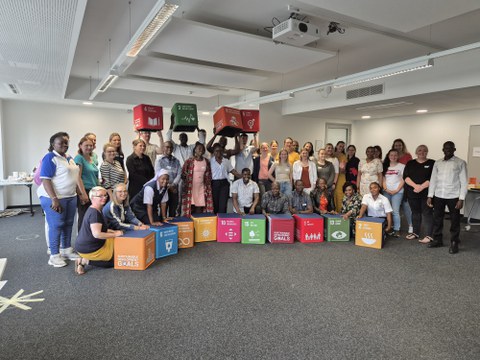Eine Gruppe von ca. 20 Personen stehen und sitzen hinter bunten Würfeln für ein Gruppenfoto