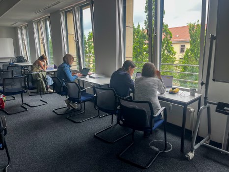 Personen sitzen an Tischen am Fenster und arbeiten einzeln an Aufgaben