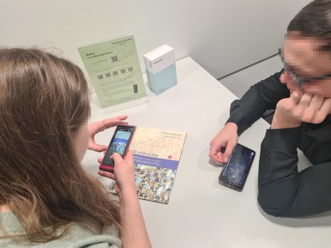 Junge Frau und junger Mann schauen Video auf ihrem Smartphone und arbeiten dabei mit einem Buch