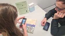 Junge Frau und junger Mann schauen Video auf ihrem Smartphone und arbeiten dabei mit einem Buch