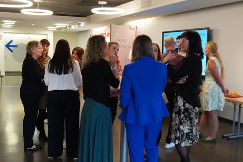 Gruppe von ca. 10 Frauen stehen in Kleingrüppchen in einem Foyer und unterhalten sich