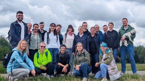 Gruppenbild mit ca. 20 Personen im Freien auf einer Wiese bei grauem Wetter