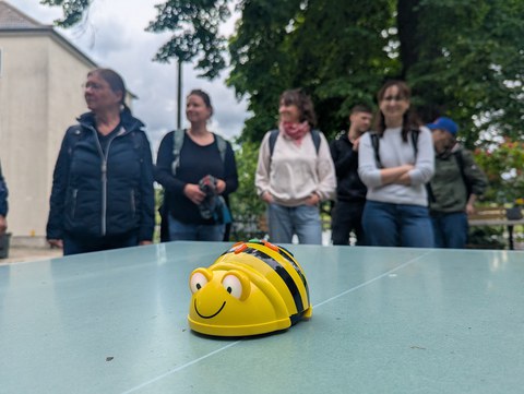 Kleiner Lernroboter in Form einer Biene, der von Leuten im Hintergrund bestaunt wird.