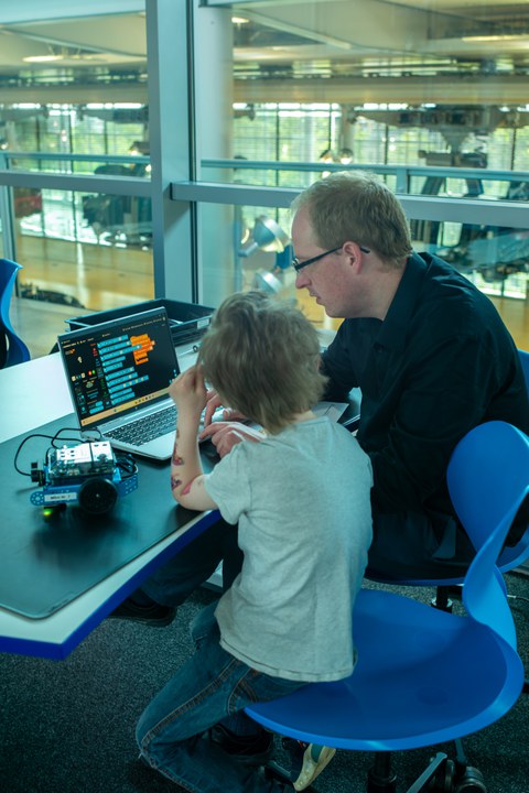 Erwachsener und Kind sitzen vor einem Laptop und programmieren einen kleinen Roboter