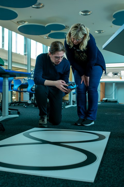 Mann udn Frau haben kleinen Roboter in der Hand und bereiten ihn auf eine Testfahrt vor