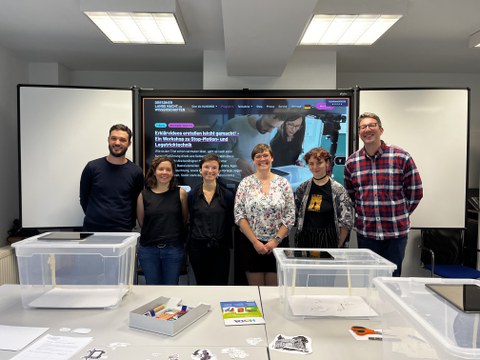 Auf dem Bild ist das 6-köpfige Team von BQL.Digital, das den Erklärvideo-Workshop zur Langen Nacht der Wissenschaften 2024 im Medienlabor angeboten hat. Sie stehen vor einer Interaktiven Tafel. Im Vordergrund sieht man mehrere Trickfilmboxen auf Tischen.