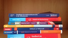 Bild von verschiedenen Mathematikbüchern, die in einem Holzregal gestapelt sind.