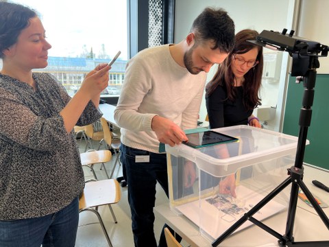 Auf dem Bild sieht man drei Dozierende bei einem Erklärvideo-Workshop, die in einer Trickbox ein Legetechnik-Video erstellen.