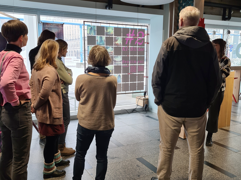 Auf dem Bild sind BQL-Teilnehmende bei der COSMO-Ausstellung im Kulturpalast Dresden zu sehen, wie sie die Ausstellungsstücke zur Künstlichen Intelligenz betrachten und der Dozentin zuhören.
