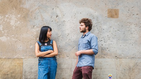 Eine asiatische Frau und ein Mann lehnen an einer Betonwand und unterhalten sich.