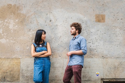Eine asiatische Frau und ein Mann lehnen an einer Betonwand und unterhalten sich.
