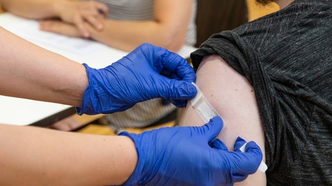 Pflaster auf der Einstichstelle am Arm einer Person (Impfung)